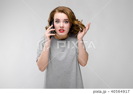 Charming young girl in a gray T-shirt on a gray background. The girl speaks by phone 40564917
