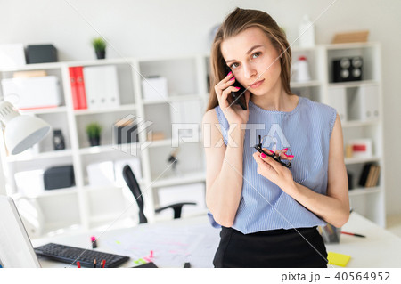 Beautiful Young girl in the office is standing near the table, holding glasses in her hand and Beautiful Young girl in the office is standing near the table, holding glasses in her hand and 40564952