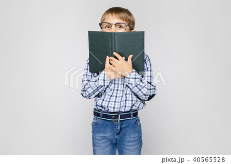 A charming boy with an inlaid shirt and light jeans stands on a gray background. The boy closed his 40565528