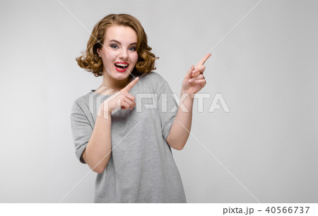 Charming young girl in a gray T-shirt on a gray background. The girl points fingers upward 40566737