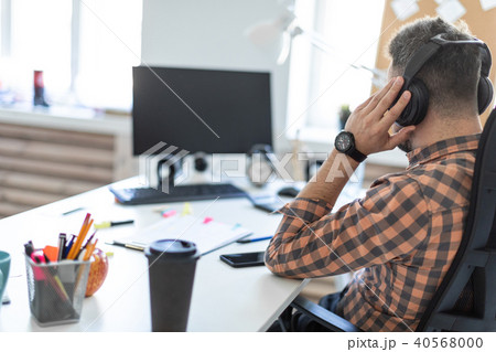 A young man in headphones sits at a table in the office and looks at the monitor. The picture is 40568000