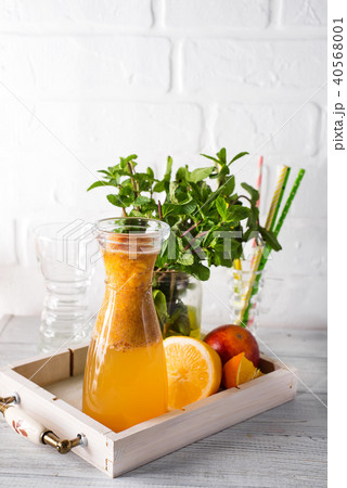 Orange lemonade in the decanter on a wooden tray with ftuits and mint 40568001