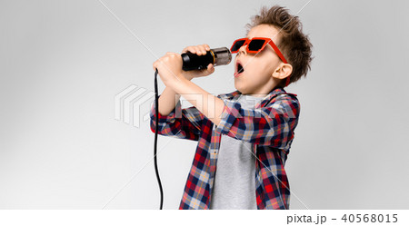 A handsome boy in a plaid shirt, gray shirt and jeans stands on a gray background. A boy wearing A handsome boy in a plaid shirt, gray shirt and jeans stands on a gray background. A boy wearing 40568015