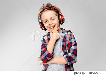 A handsome boy in a plaid shirt, gray shirt and jeans stands on a gray background. A boy in red A handsome boy in a plaid shirt, gray shirt and jeans stands on a gray background. A boy in red 40568028