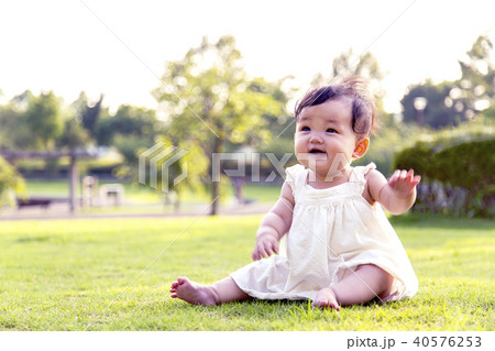 公園の芝生の上に座り一人遊ぶ女の子の赤ちゃんの写真素材
