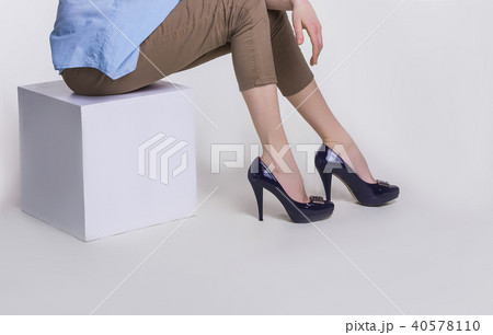 Legs of slim young woman in stylish high-heeled shoes sitting on white background Legs of slim young woman in stylish high-heeled shoes sitting on white background 40578110