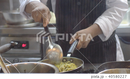 Hands of Professional chef stirs spaghetti on a pan. Cook works in a modern kitchen with lots of Hands of Professional chef stirs spaghetti on a pan. Cook works in a modern kitchen with lots of 40580227