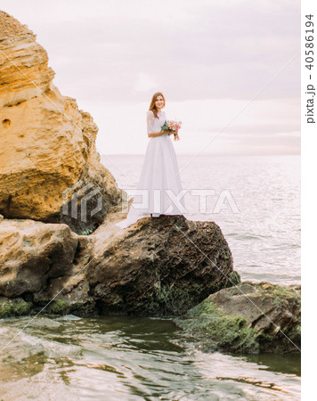 The full-length photo of the standing on the cliff bride at the background of the sea. 40586194