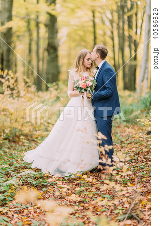 Full-length photo of the groom kissing the bride in the forehead in the autumn forest. Full-length photo of the groom kissing the bride in the forehead in the autumn forest. 40586329