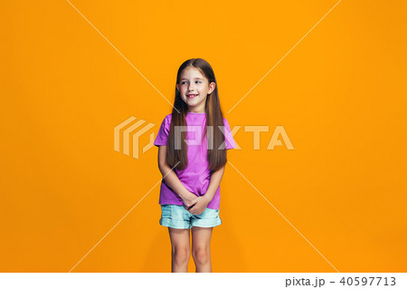 The happy teen girl standing and smiling against orange background. 40597713