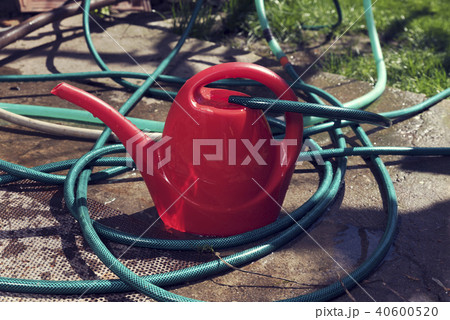 Red water can filling with water with green hose Red water can filling with water with green hose 40600520