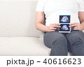 Pregnant woman sitting on sofa holding ultrasound. 40616623