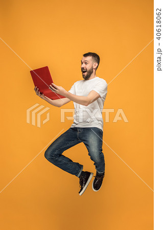 Image of young man over orange background using laptop computer while jumping. Image of young man over orange background using laptop computer while jumping. 40618062