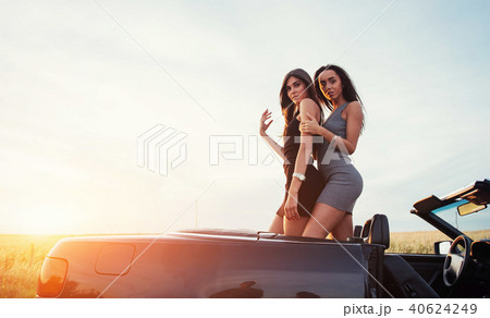 Two girls happy to pose next a black car Two girls happy to pose next a black car 40624249