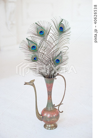 Vintage ancient copper jug on white table decorated with big peacock feather Vintage ancient copper jug on white table decorated with big peacock feather 40626538