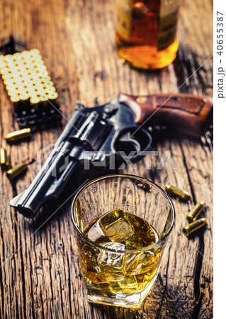 Glass of whiskey cognac or bourbon with revolver. Glass of whiskey cognac or bourbon with revolver. 40655387