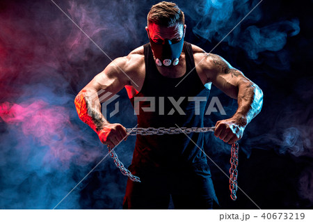 Portrait of muscular sportsman tearing metal chain. Black background with smoke 40673219