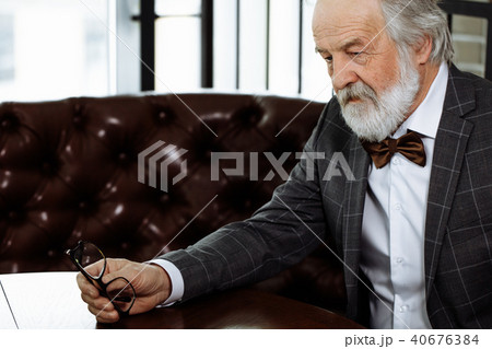 unhappy old person holding his glasses and sitting on the red couch 40676384