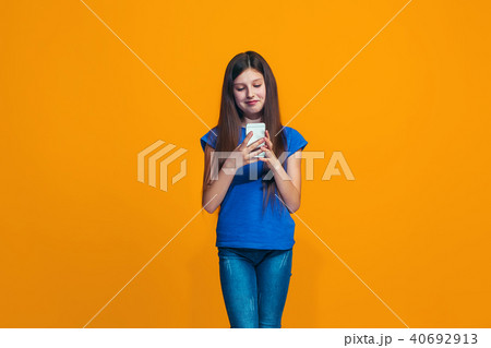 The happy teen girl standing and smiling against orange background. 40692913