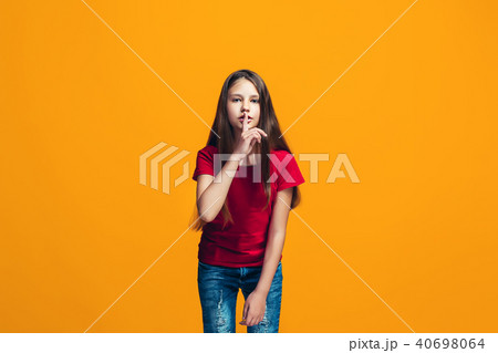 The young teen girl whispering a secret behind her hand over orange background The young teen girl whispering a secret behind her hand over orange background 40698064