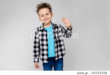 A handsome boy in a plaid shirt, blue shirt and jeans stands on a gray background. The boy smiles 40703308