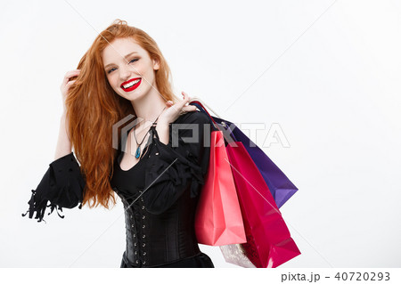 Halloween witch concept - Happy Halloween Witch smiling and holding colorful shopping bags on white 40720293