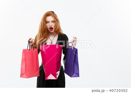 Halloween witch concept - Happy Halloween Witch smiling and holding colorful shopping bags on white 40720302