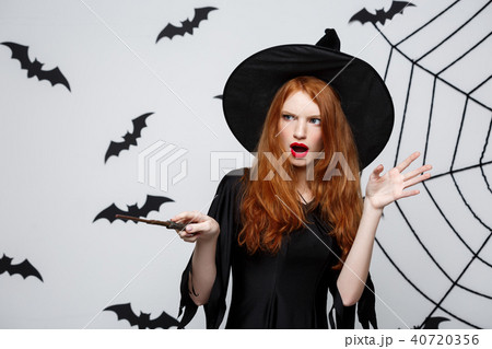 Halloween Concept - Beautiful Witch playing with magic stick on grey background. 40720356