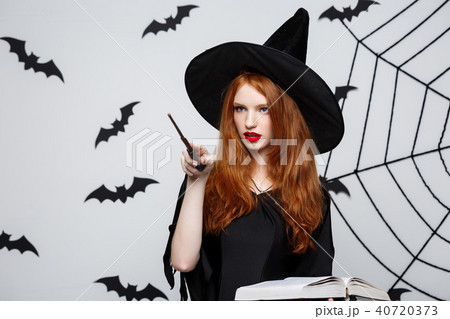 Halloween Concept - Beautiful Witch playing with magic stick on grey background. 40720373