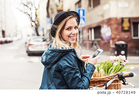 Young woman with bicycle and smartphone in sunny spring town. 40728149