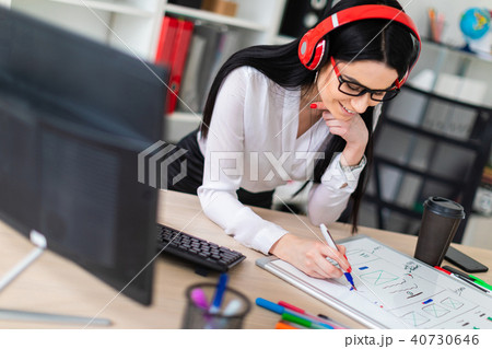 A young girl in the headphones stands near the table and draws a marker on a magnetic board. 40730646