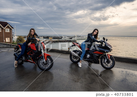 Two Biker girls in leather jackets on a black and red color sport motorcycles Two Biker girls in leather jackets on a black and red color sport motorcycles 40733801