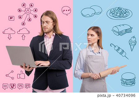 Serious housewife holding a rolling pin and looking at her working husband 40734096