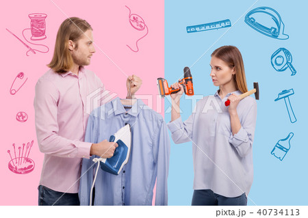 Man with an iron feeling surprised while seeing his wife holding instruments Man with an iron feeling surprised while seeing his wife holding instruments 40734113