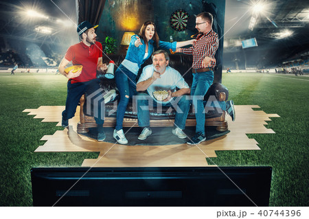Soccer football fans sitting on the sofa and watching TV in the middle of a football field. Soccer football fans sitting on the sofa and watching TV in the middle of a football field. 40744396