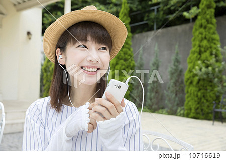 スマホで音楽を聴く若い女性 夏服 屋外の写真素材