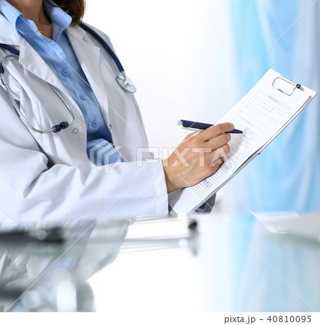 Female doctor filling up medical form on clipboard, closeup. Reflecting glass table is a physician 40810095