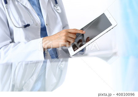 Woman doctor using tablet computer while sitting. Reflecting glass table is a working place of 40810096
