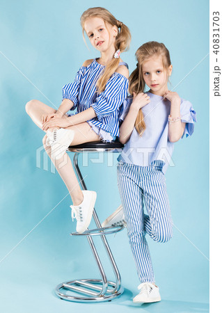 Girls twins in light blue clothes are posing near a bar stool on a blue background. Girls twins in light blue clothes are posing near a bar stool on a blue background. 40831703