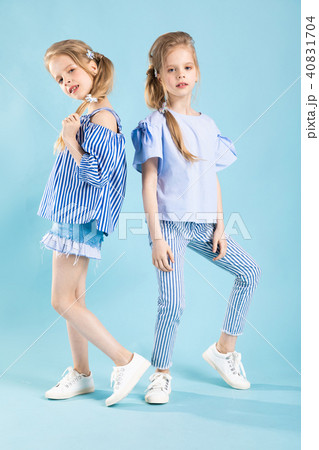 Girls twins in light blue clothes are posing on a blue background. Girls twins in light blue clothes are posing on a blue background. 40831704