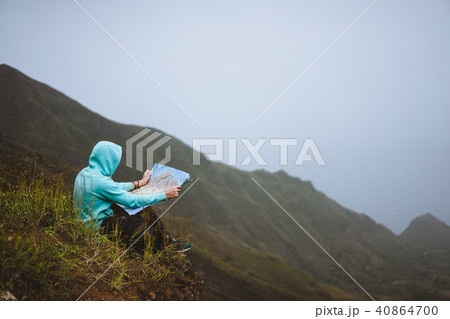 Traveler wear blue hoodie with the map sitting on the hill of a mountain in front of a gorgeous Traveler wear blue hoodie with the map sitting on the hill of a mountain in front of a gorgeous 40864700