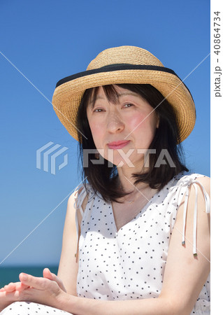 砂浜の海岸で快晴の青空をバックに白いワンピースにストローハットの女性のポートレートを撮影 40864734