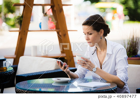 Portrait of young businesswoman drinking coffee and using mobile phone while sitting at the sidewalk 40897477