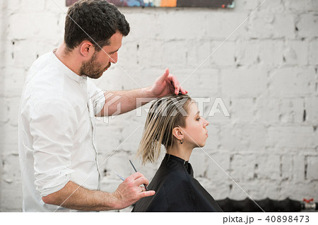 hairdresser cuts hair with scissors on crown of handsome satisfied client in professional hairdresser cuts hair with scissors on crown of handsome satisfied client in professional 40898473