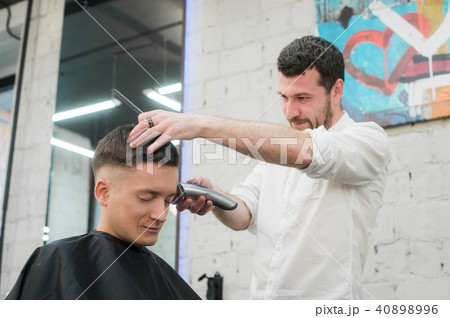 Professional styling. Close up side view of young satisfied man getting haircut by hairdresser with 40898996