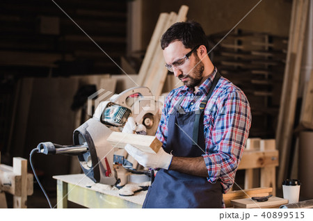 Handsome carpenter in protective glasses standing near his wooden object in the workshop Handsome carpenter in protective glasses standing near his wooden object in the workshop 40899515
