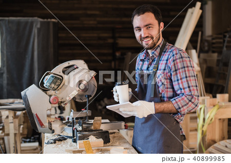 Carpenter taking a coffee break holding notebook in front of circular saw at his workshop Carpenter taking a coffee break holding notebook in front of circular saw at his workshop 40899985