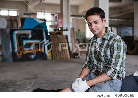 Handsome carpenter in protective glasses is looking at camera and smiling while standing near his 40900069