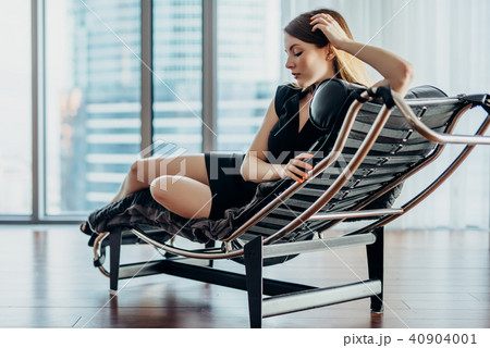 Portrait of female model wearing short black dress and high heels relaxing on chair 40904001