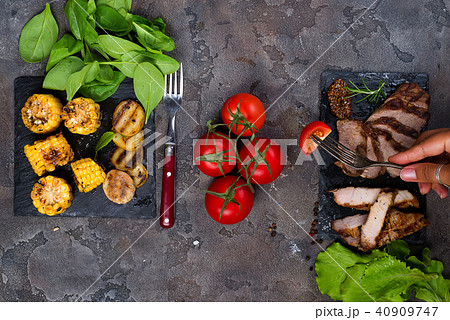 female hand holds a fork with slice tomato on the background fresh three types of grilled steak on female hand holds a fork with slice tomato on the background fresh three types of grilled steak on 40909747